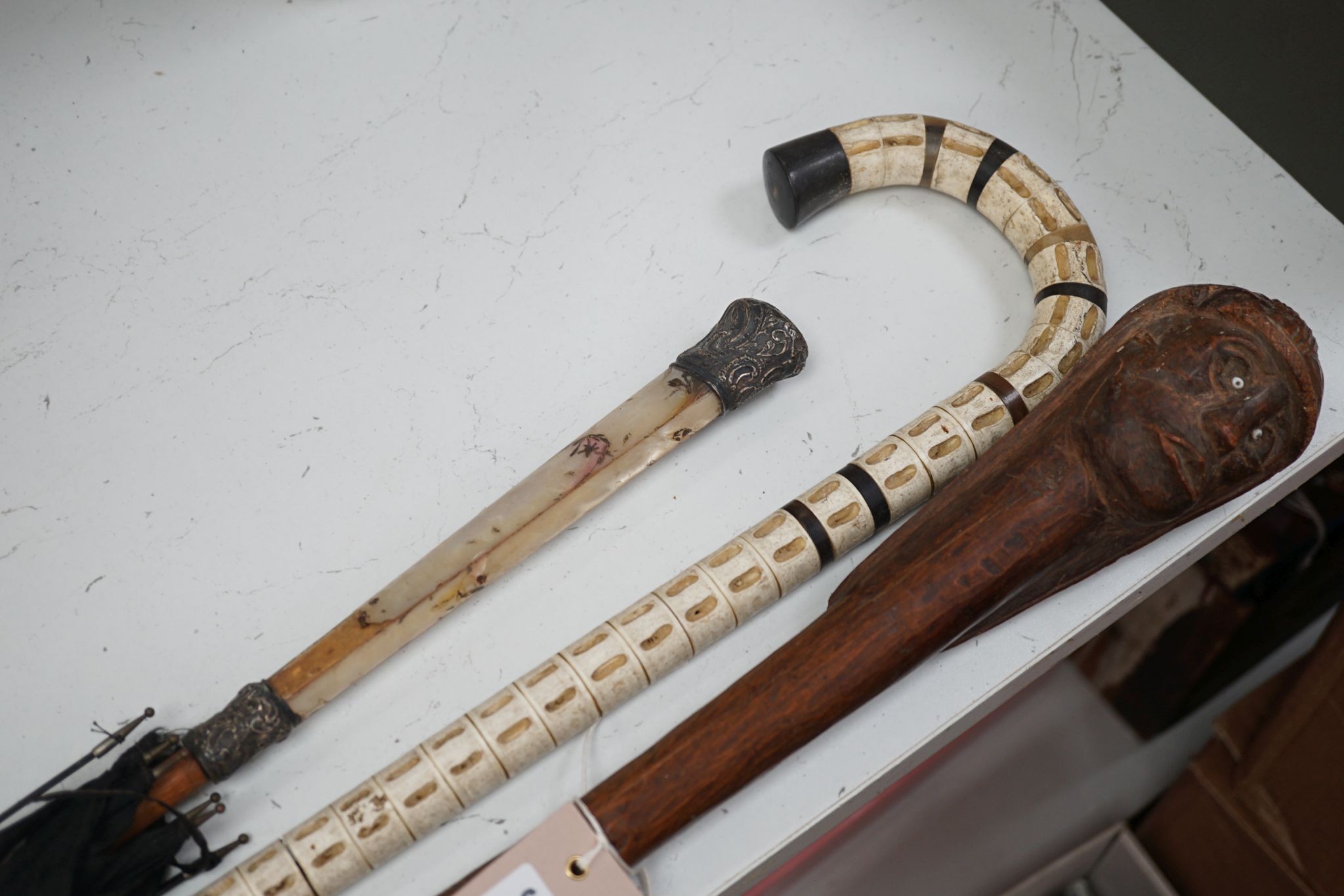 A carved wood figural walking cane, a vertebrae walking stick and a Victorian parasol. Longest 108cm